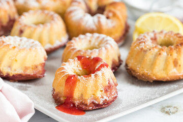 Mini bundt cakes in lemon flavor with strawberry sauce served on white plate