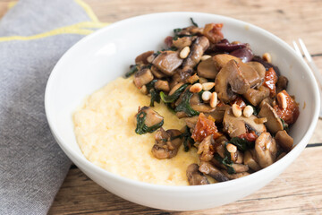 Creamy polenta with mushroom and spinach stir-fry, served in white plate. Plant-based main dish