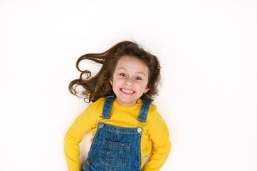 Charming European 5-6 years little child girl, in yellow sweater and blue denim overalls, smiles a...