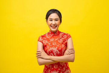 Beautiful Asian woman wearing traditional cheongsam with arms crossed isolated on yellow background, Happy Chinese New Year.