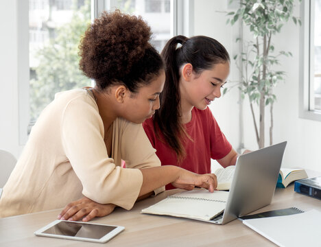 Multiracial group of girl students sitting at table studying in classroom. Young diverse ethnic schoolgirls using laptop computer and writing homework.Teenager education and back to school concept.