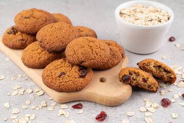 Oatmeal cookies on a wooden board, oatmeal and dried cranberries on a gray table.