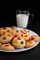 In the foreground is a blurry image of a cookie in a plate, and in the background is a cup of milk on a dark background.