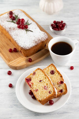 Blurred image of a cupcake with cranberries and a cup of coffee on a light table.