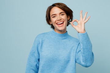 Young satisfied smiling happy fun caucasian woman wear knitted sweater look camera showing okay ok gesture isolated on plain pastel light blue cyan background studio portrait People lifestyle concept - obrazy, fototapety, plakaty
