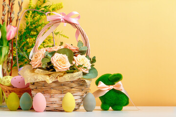 Easter still life. A basket with flowers and eggs, a toy rabbit on the table. copy space