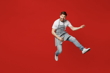 Fototapeta na wymiar Full body musician fun young male housewife housekeeper chef cook baker man wear grey apron jump high pov playing guitar do hand gesture isolated on plain red background studio. Cooking food concept