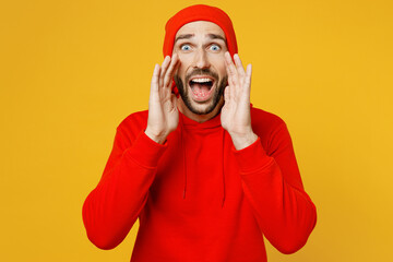 Young promoter caucasian man wear red hoody hat scream sharing hot news about sales discount with hands near mouth isolated on plain yellow color background studio portrait. People lifestyle concept.