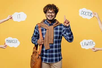 Young teen Indian boy student wearing casual clothes glasses bag near card with doctor manager lawyer IT text choose profession point finger up isolated on plain yellow background University concept.