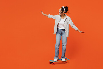 Full body fun young woman of African American ethnicity she wears grey shirt headband learn riding skateboard pennyboard isolated on plain orange background studio portrait. People lifestyle concept. - Powered by Adobe