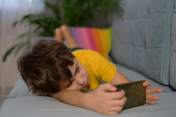 frustrating boy, looking bored, playing on the phone. sleepy boy playing on the phone lying on the couch. kids and gadgets concept