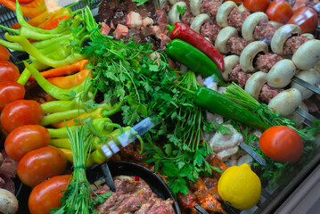 Meat raw products on skewers ready for cooking, laid out among vegetables and fresh herbs
