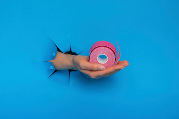 hand with pink kinesiology tape on a blue background. Physiotherapy and therapeutic tape for wrist pain, aches and tension. elastic therapeutic tape.