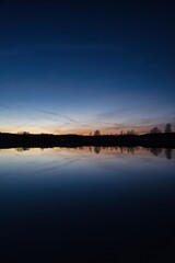 Wonderful blue golden red sky after sunset with trees in foreground at a lake with its reflections 