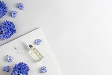 Facial serum in glass dropper bottle on marble podium with blue hyacinth flowers on light grey...