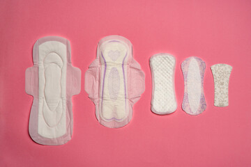 Four different types of sanitary pads for woman, on pink background.