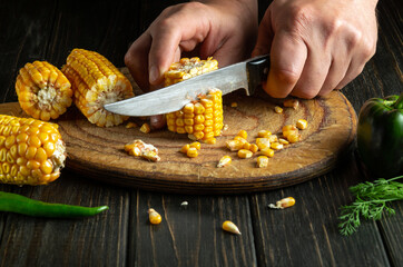 Close-up of a cook hands with a knife cut corn on a cutting board. Cooking vegetarian food on the restaurant kitchen table