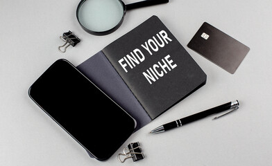 FIND YOUR NICHE text written on black notebook with smartphone, magnifier and credit card