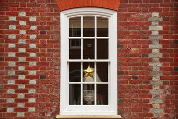 Fototapeta na wymiar Beautiful Christmas decoration placed in front of a white wooden window on a brick facade building. British English architecture house design.