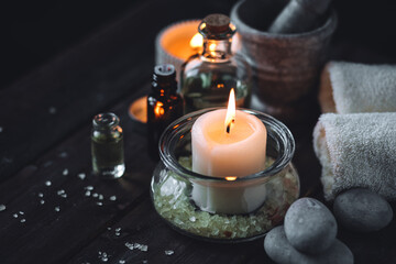 Spa setting with essential oil, candle, sea salt, pebbles, towel on dark wooden background. Massage, aromatherapy. Natural organic ingredients for relaxation, detention. Wellness in salon concept