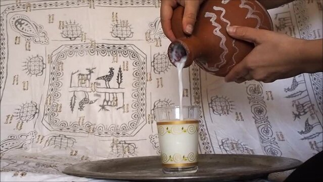 Filling buttermilk (ayran) from clay jug to the glass. Turkish traditional drink, ayran in the pot (testi). Anatolian motifs, Turkish patterns.