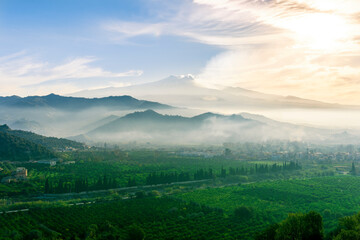 Obraz premium view at beautiful misty spring mountain valley with green gardens and mountains in mist on background of landscape