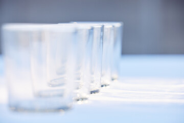 Glass, crockery and mockup with a row of drinking glasses on a table in a studio or restaurant for...