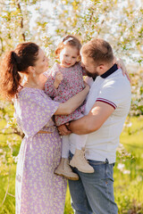happy family. a mom and a dad with a baby daughter in a blooming spring garden. 