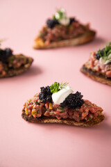 Tatar Canapé vom Rind mit Schmand, Kaviar, Dill als Vorspeisen Fingerfood Häppchen auf rosa pink Hintergrund