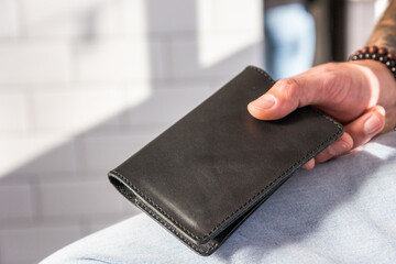 Migration and citizenship. Man's hand holds passport in black leather cover, close-up. Handmade...