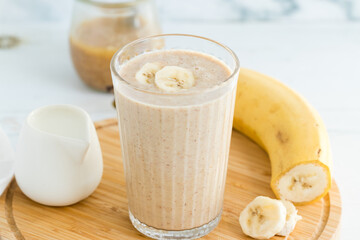 A glass of banana nut butter smoothie served on a wooden cutting board