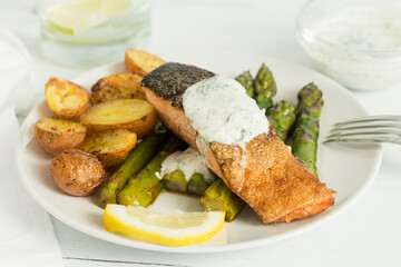 One plate of roasted salmon  with steak potatoes, asparagus, yogurt sauce and lemon.