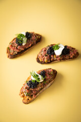 Tatar Canapé vom Rind mit Schmand, Kaviar, Dill als Vorspeisen Fingerfood Häppchen auf pastell gelb Hintergrund