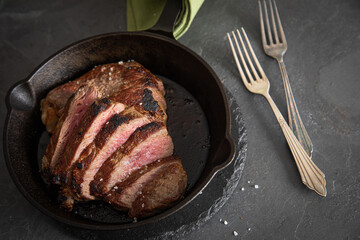 Entrecote Steak vom Rind medium rare gebraten in Gusseisen Pfanne mit Meersalz auf schwarzen Schiefer mit Gabel, grünen Tuch und dunklen Stein Hintergrund