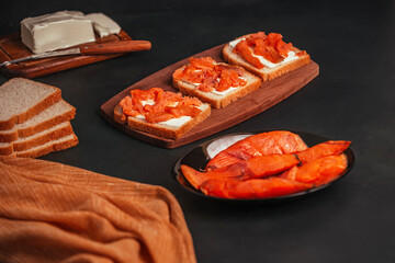 on a dark background, slices of smoked red fish and sandwiches with it are laid out in a plate