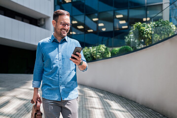 Smiling adult businessman, receiving a lovely message on his phone while walking.
