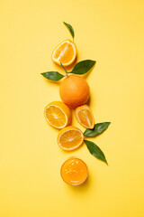 Orange fruit top view with slices and glass of juice on yellow background.