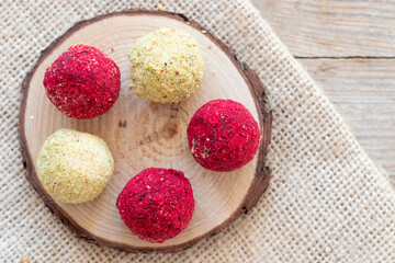 Colorful candy balls with dried raspberry, grated coconut, white chocolate and nuts, served on a piece of wood log, top view.