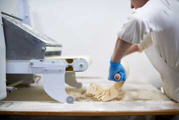 chef  processing pasta sheet in machine at kitchen. Manufacture. Rolling dough on a dought sheeter .