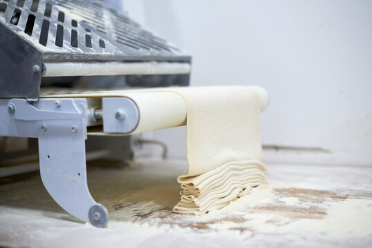 Pasta sheet in machine at kitchen. Manufacture. Rolling dough on a dought sheeter .  Bakery concept.