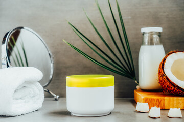 Beauty spa skincare cosmetic mockup cream package with coconut oil, fresh coconut, towel and mirror on dark gray background. Natural spa cosmetics concept. Selective focus, copy space.