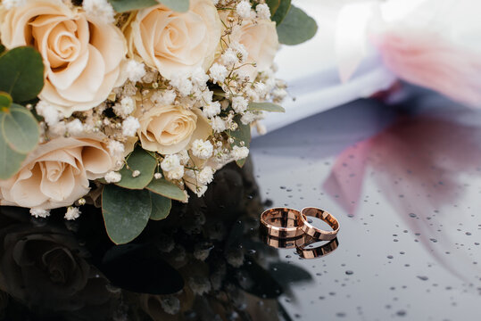 A beautiful toned picture with wedding rings lies on a black surface against the background of a bouquet of flowers