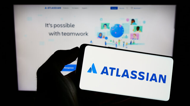 Stuttgart, Germany - 12-30-2022: Person holding smartphone with logo of Australian software company Atlassian Corporation on screen in front of website. Focus on phone display.
