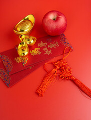 Happy Chinese New Year. Apple, Chinese Gold Sycee, angpao or red packet monetary gift for a symbol of prosperity. Isolated red. Copy space. Usable for wallpaper, greeting card, design.