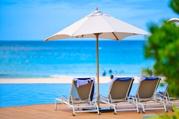 White sand beach and blue sea landscape view of a tropical resort hotel beside modern swimming pool, white parasols, palm trees, deck beach chairs in the golden sunset time