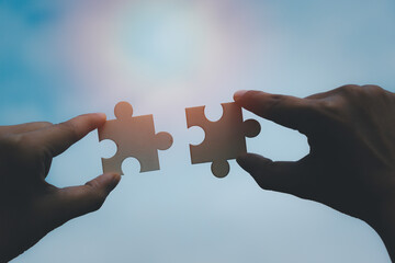 Two Hands of woman trying to connect puzzle piece with sunrise background. Jigsaw wooden against sun rays and sky one whole in middle. symbol for association teamwork business strategy and connection.