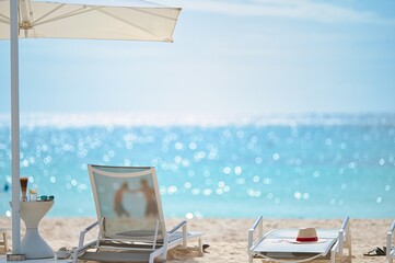 White sand beach and blue sea landscape view of a tropical resort hotel beside modern swimming pool, white parasols, palm trees, deck beach chairs in the golden sunset time