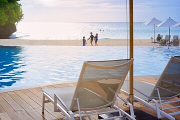 White sand beach and blue sea landscape view of a tropical resort hotel beside modern swimming pool, white parasols, palm trees, deck beach chairs in the golden sunset time