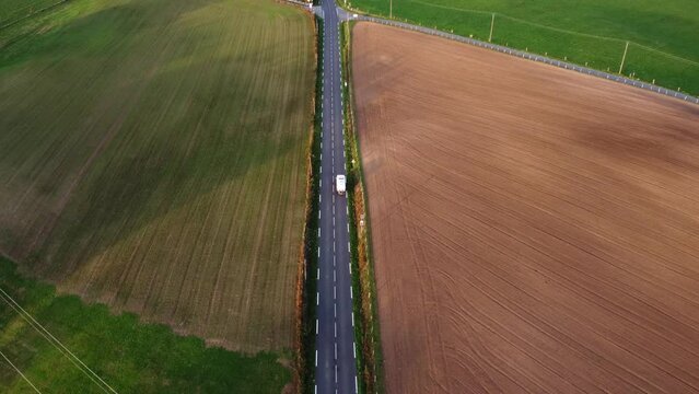 Camping car vu de haut roulant sur une grande route au milieu de divers champs et parcelles agricoles. Suivi en drone d'un voyageur.