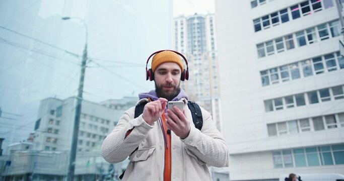 Handsome arab hipster man with beard wearing yellow hat using smartphone to listen to the music outdoors in the city streets at winter